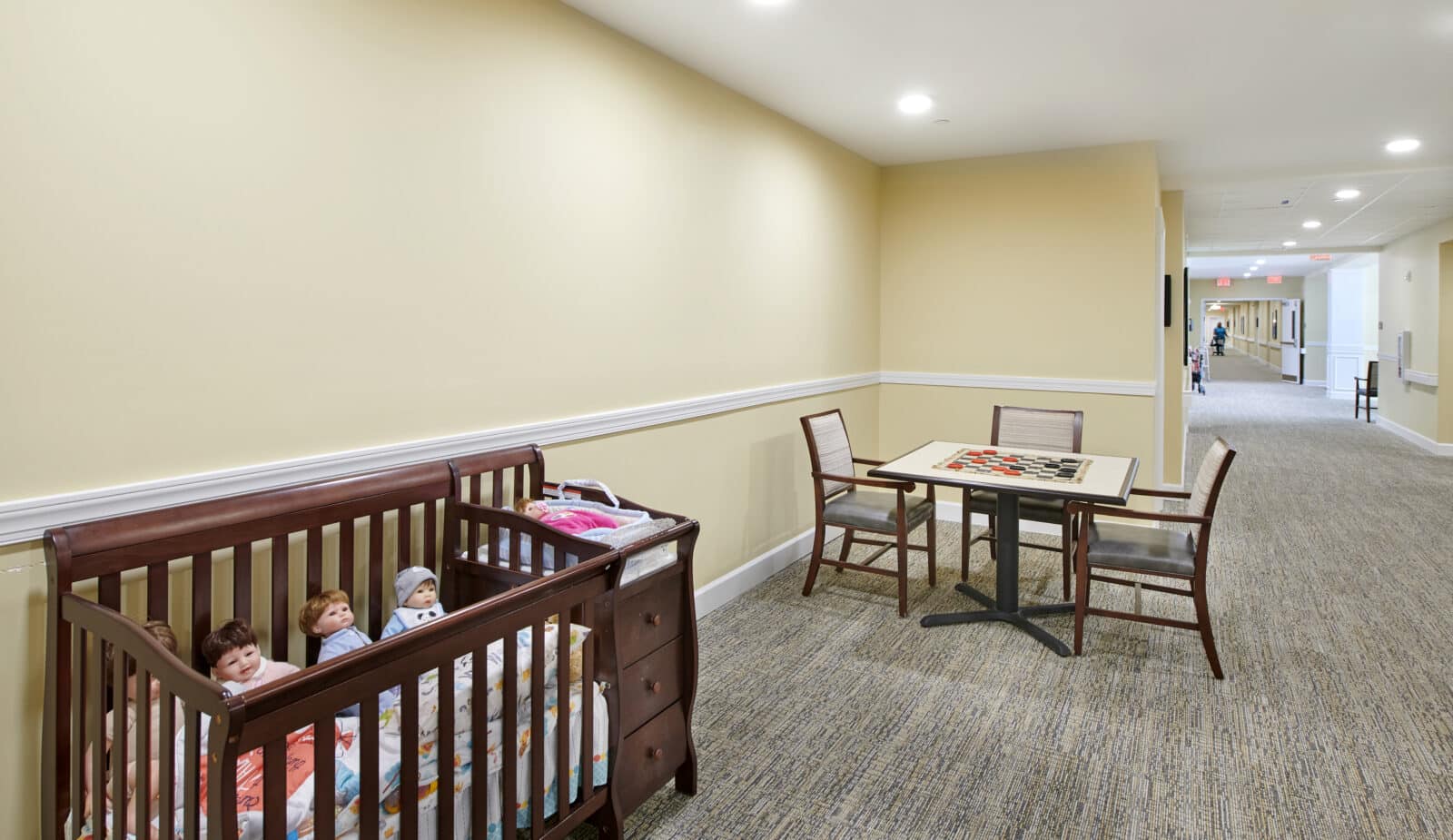 long hallway; table of checkers with three chairs and a crib with infant dolls and a changing station