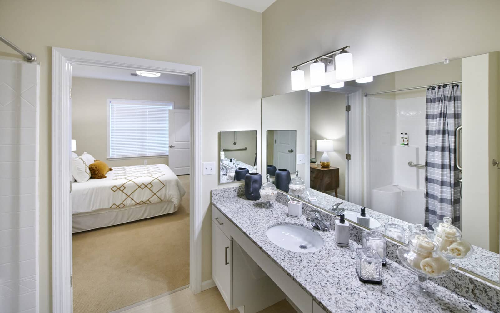 bathroom vanity with mirror; blue and white shower curtain with walk-in shower, next to bedroom with white bed cover and beige carpet