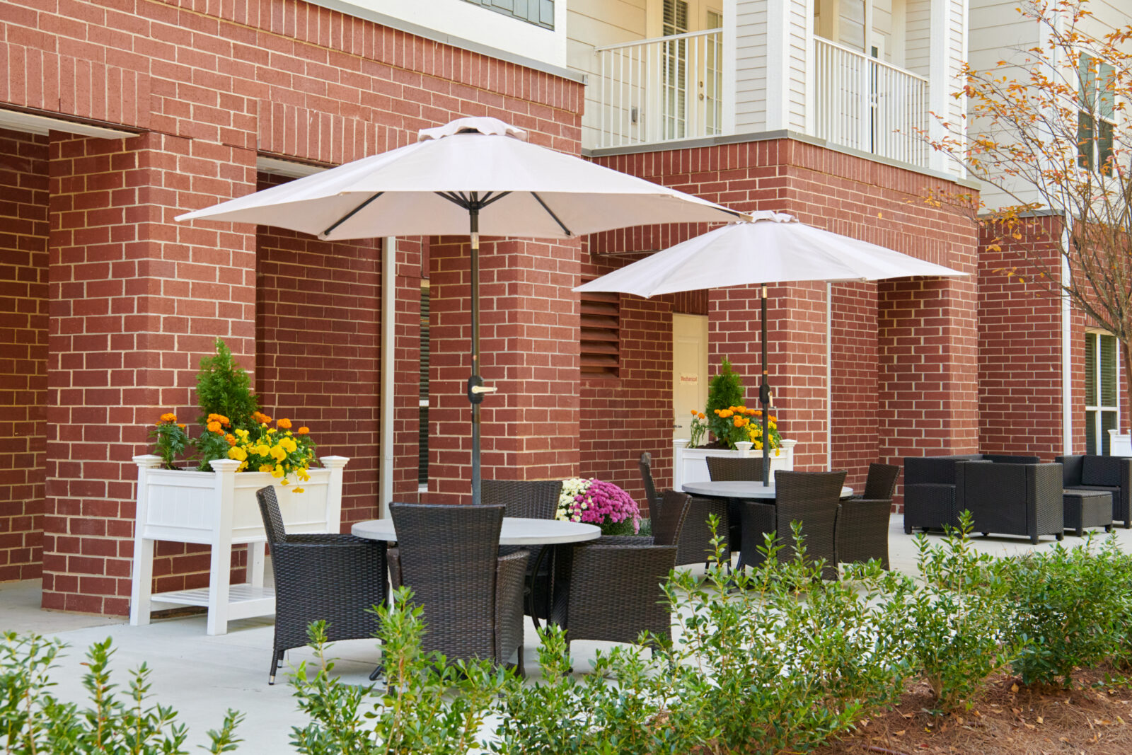 patio with seating an white umbrellas, purple, orange and yellow flowers in pots