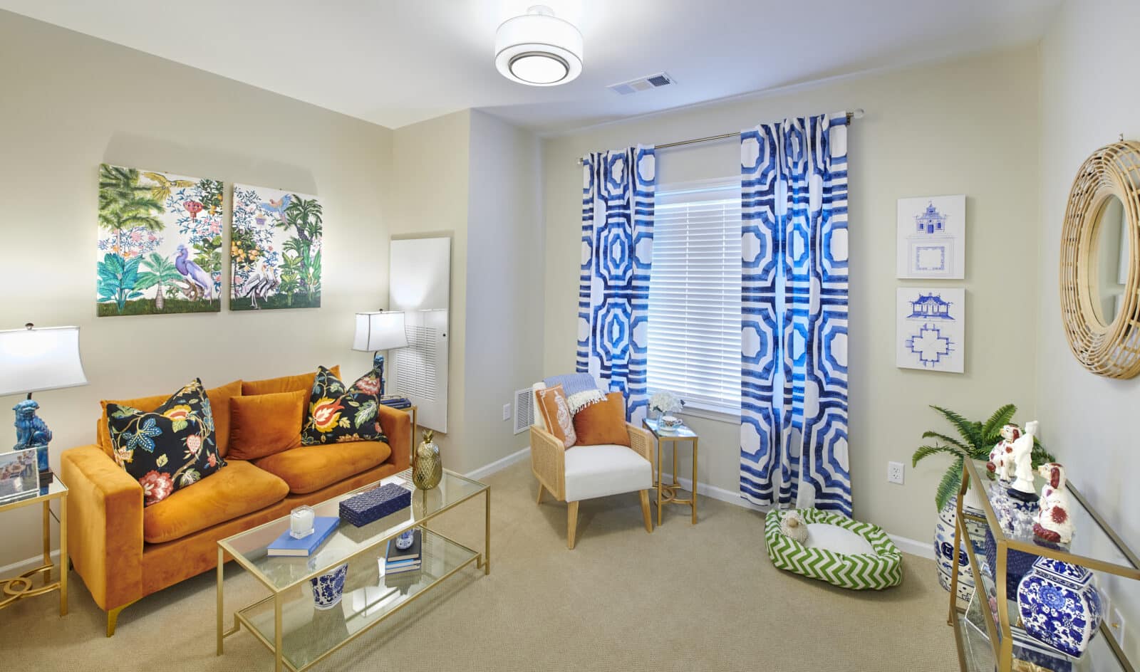 orange couch with black pillows with a color design and two prints above, blue and white window treatment